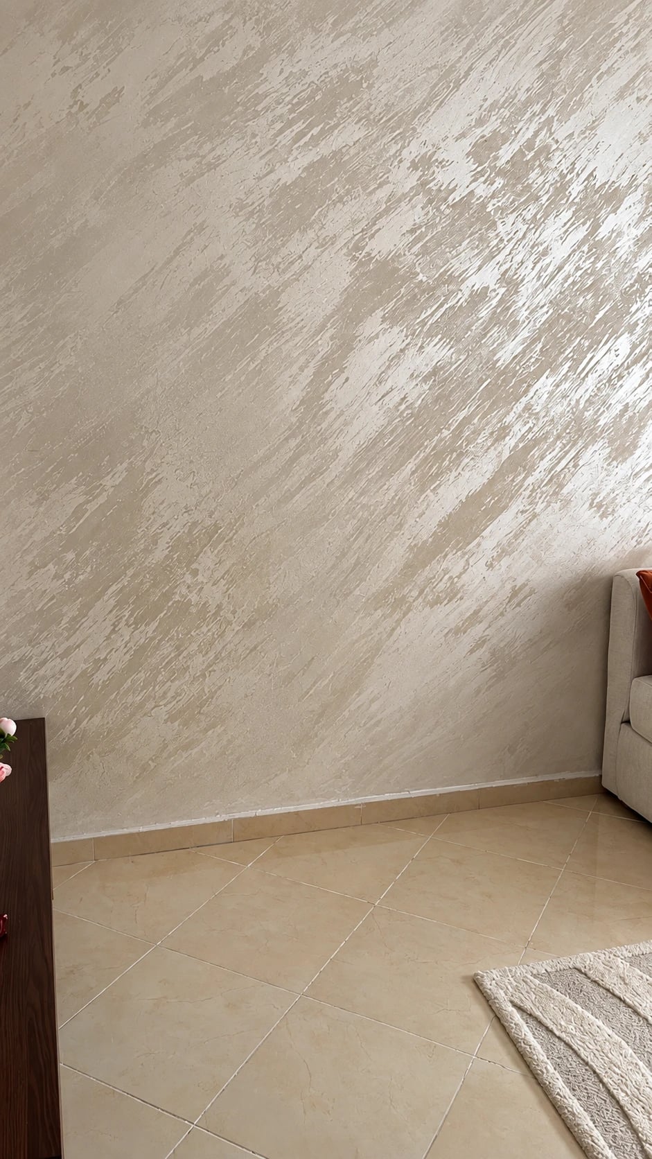 A living room wall in Swahili Effect plaster, the trowel movement sweeping diagonally across its full height, above a tiled floor.